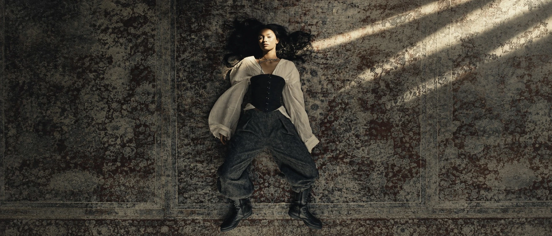 A fashion portrait in sculptural black clothing against weathered stone.