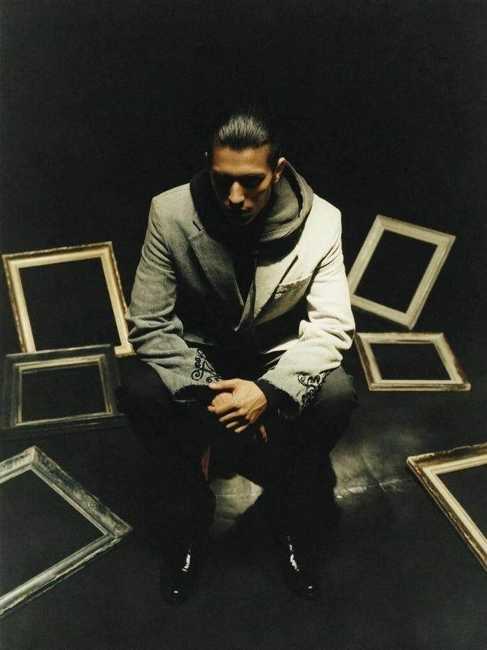 A seated figure framed by angular furniture.